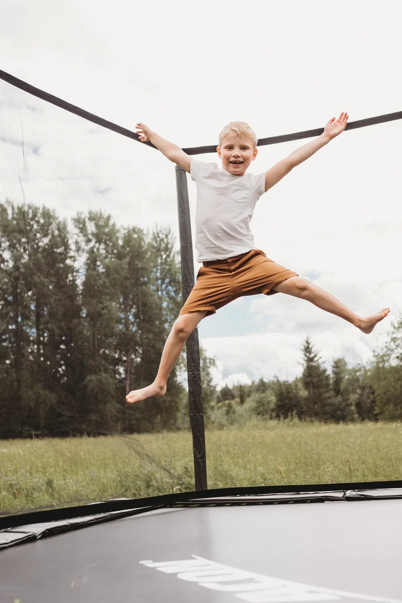 A girl performing a flip on a Acon trampoline, while two other children watch in the background.