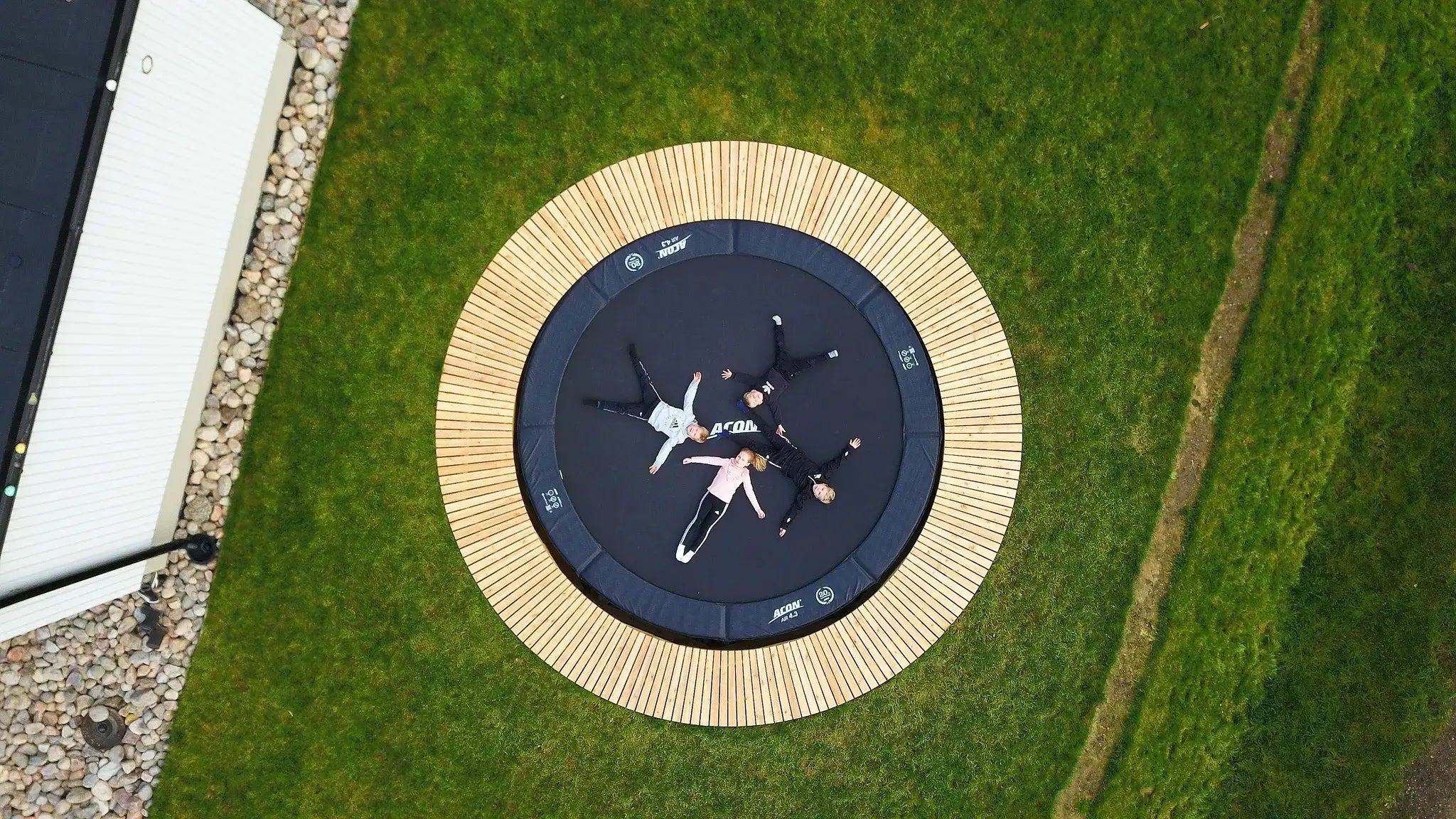 Four kids laying on a round in-gound Acon trampoline, surrounded by green grass.