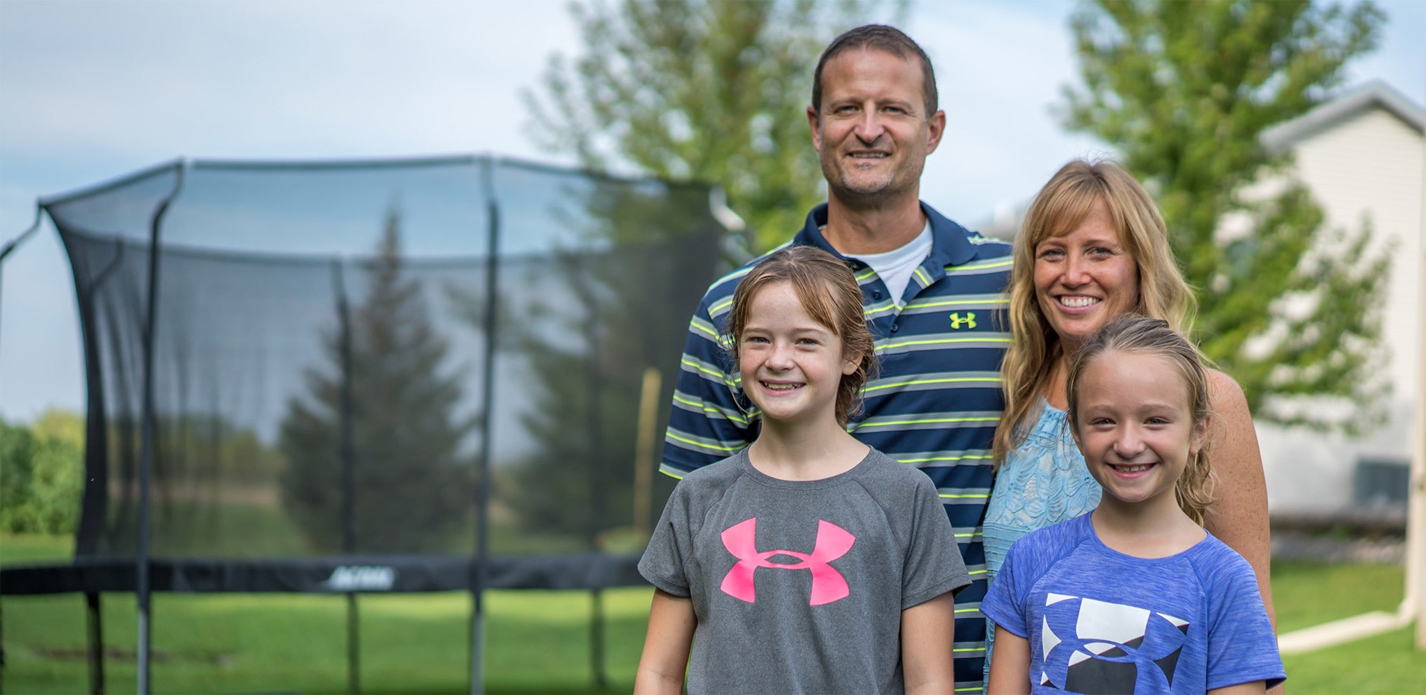 Acon customer family with a father and mother as well as two girls. There is a round ACON trampoline with net on the background.