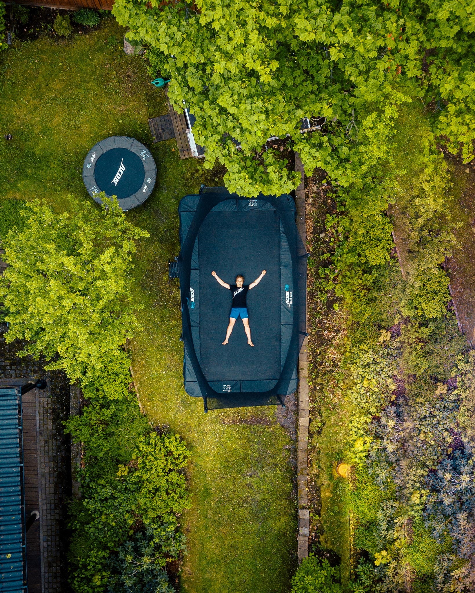 A boy lying on Acon 16 Sport HD trampoline in a backyard, seen above