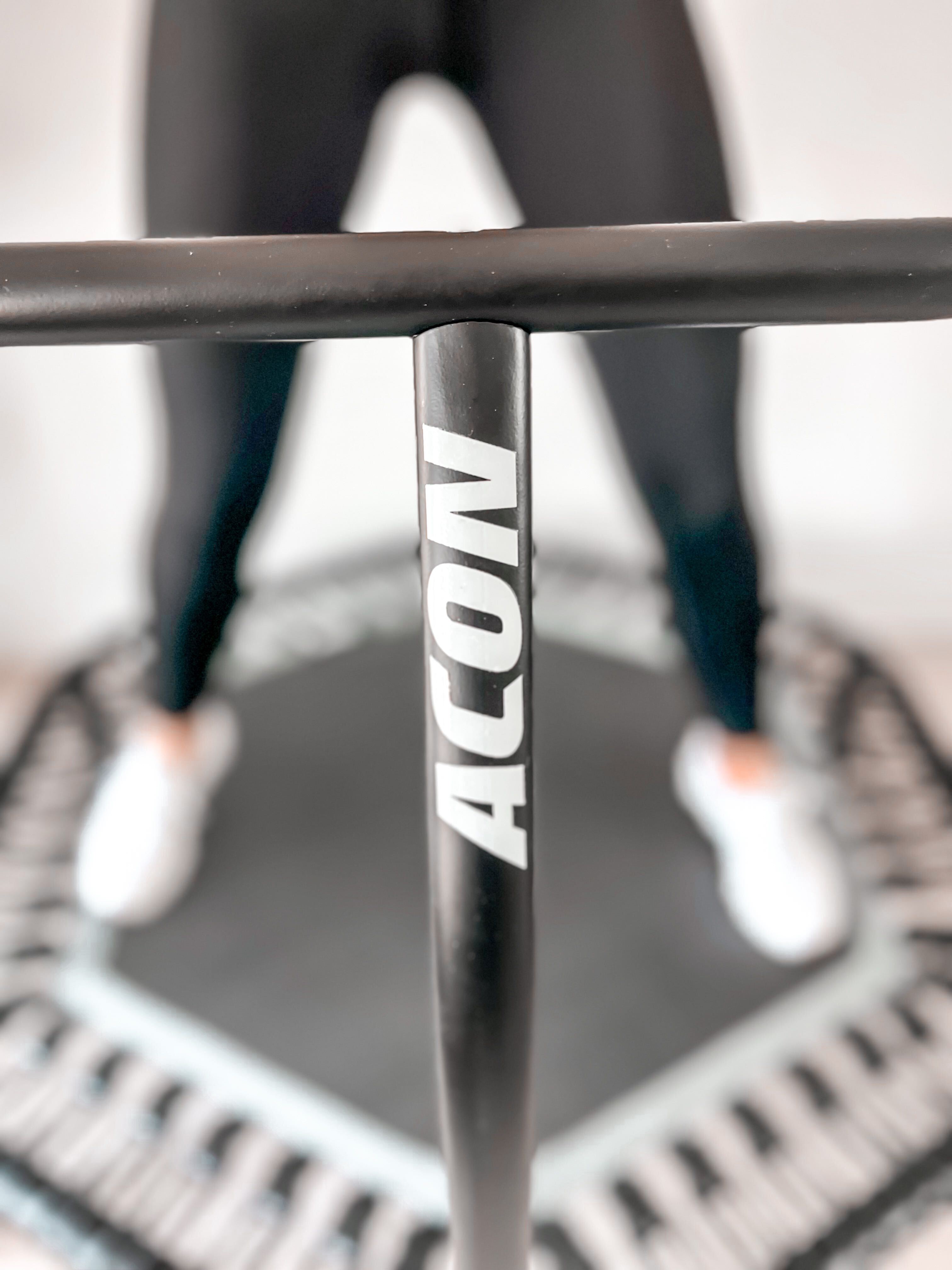 A closeup of a rebounder with handlebar. The rebounder is black with white ACON logo