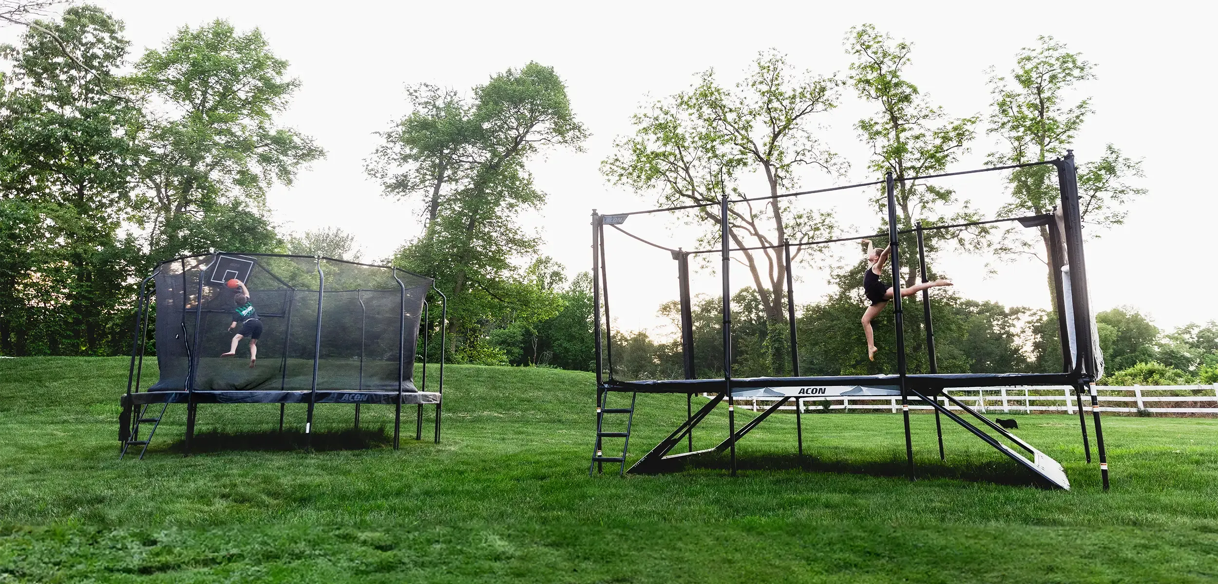 A boy plays trampoline basketball on an Acon Air, while a girl performs a skill jump on an Acon X in a lush, green garden.