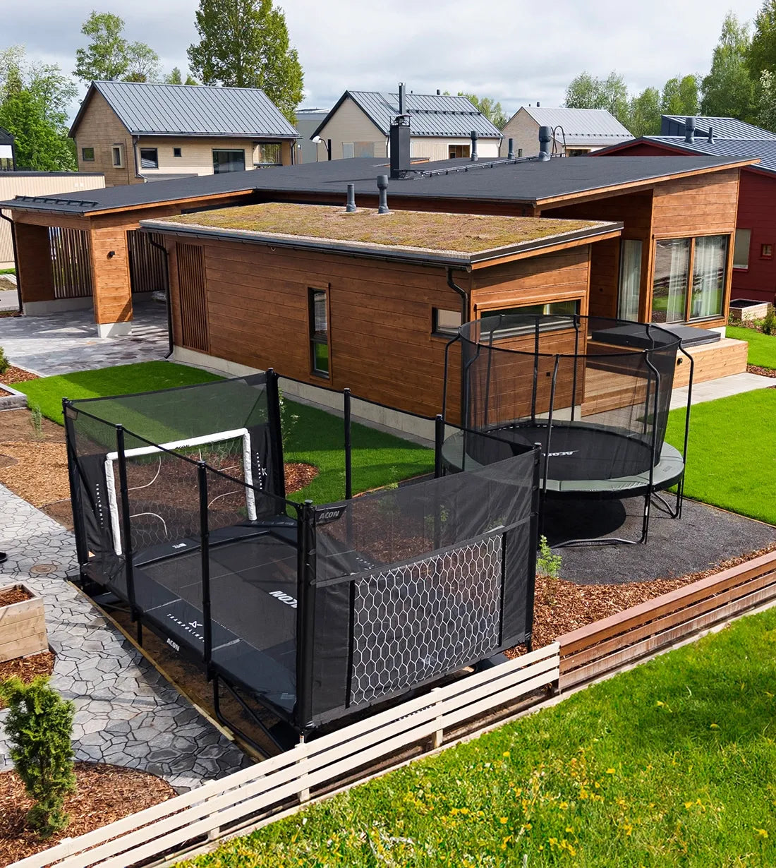 Two Acon trampolines in the backyard of a modern house. One is partially sunken trampoline inground.