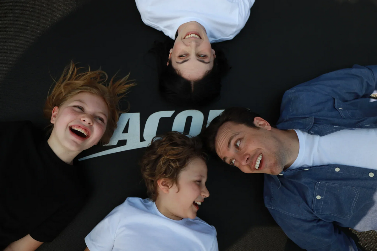 Happy family of four laying on a Acon trampoline and smiling at each others. 