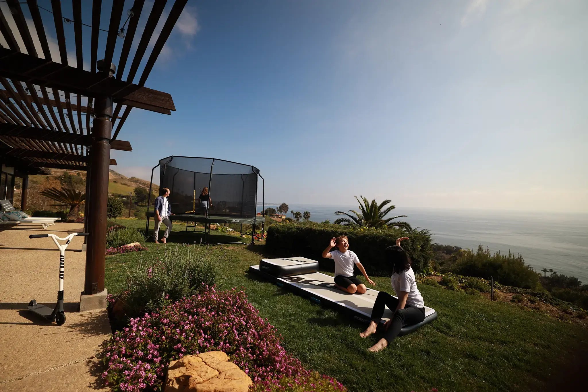 Family outside spending time together, mom high fiving son on the Acon air roll, while dad watches daughter jumping on a Acon trampoline. 