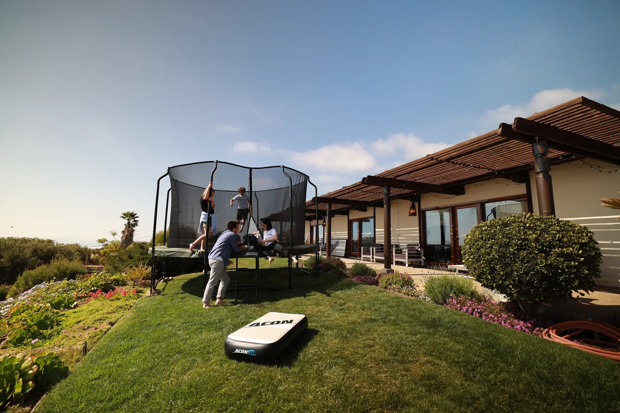 Family enjoying an Acon trampoline in a sunny backyard.