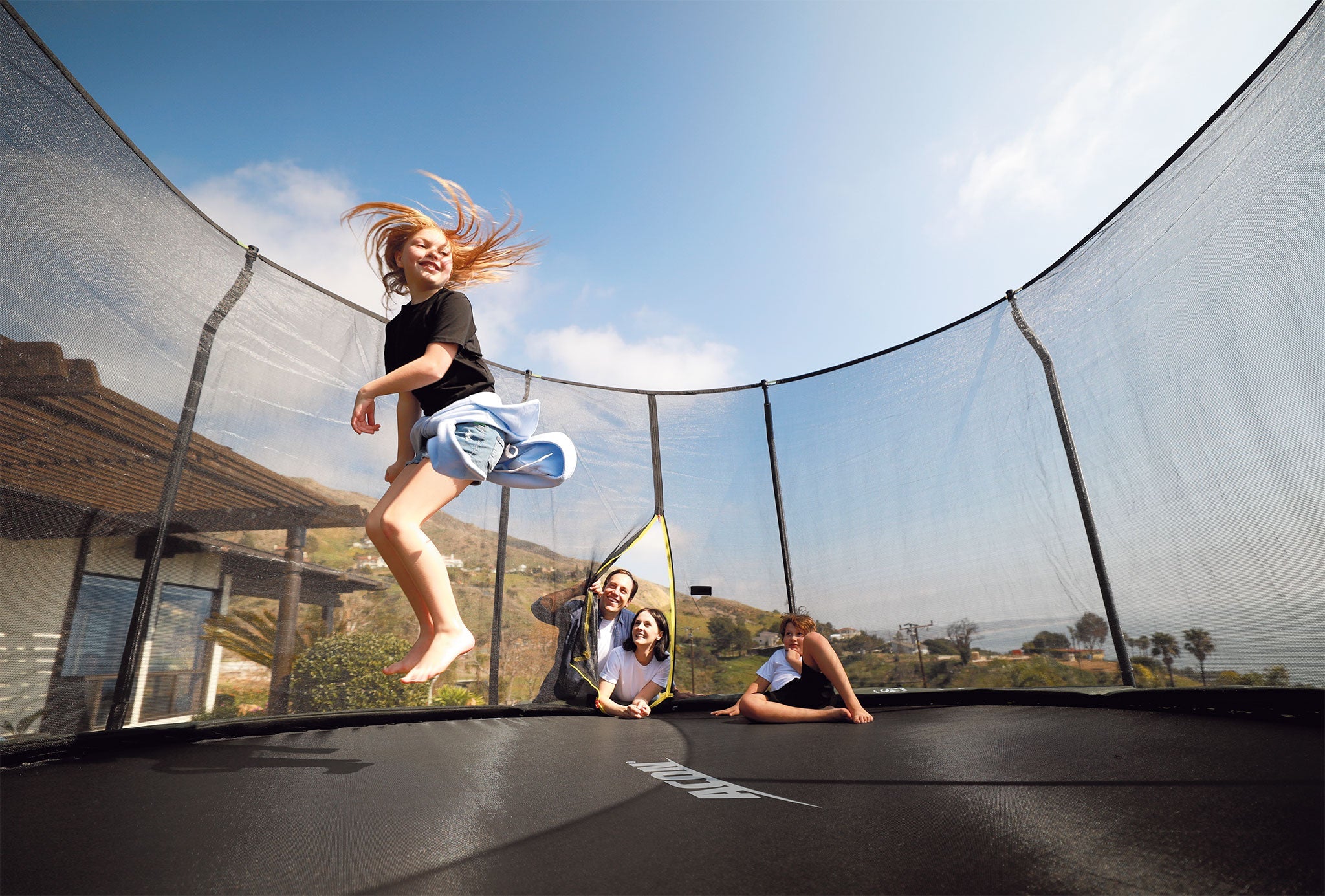Family watching the girl jumping on the safest trampoline with safety net