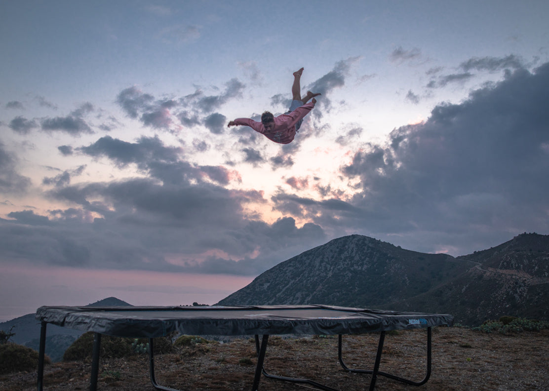 A guy jumping high on a Acon 16HD trampoline in a Grecian landscape