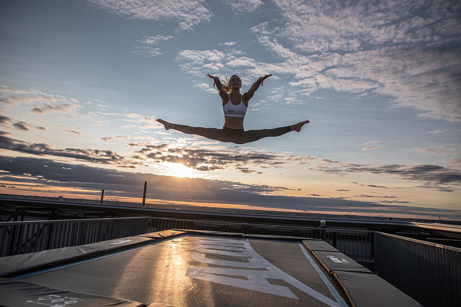 A fit woman jumping on a big trampoline with sunset as a background.