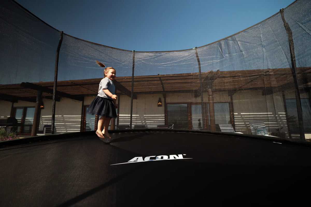 Young toddler jumping on a round Acon trampoline with safety net. 