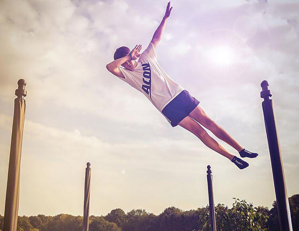 A man doing a trick on a trampoline with Acon t-shirt