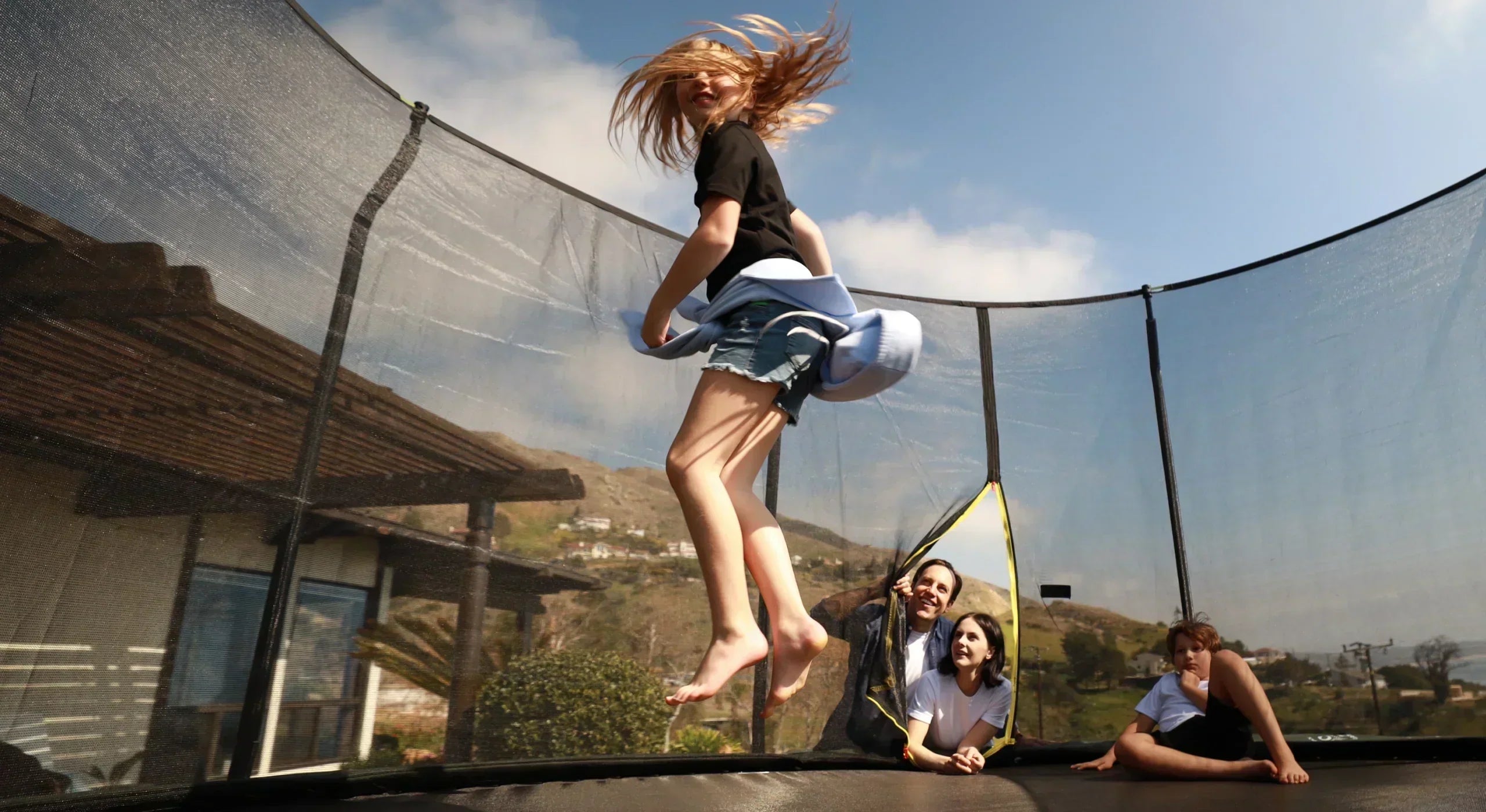 Gilr jumping on a trampoline while her parents watch from the side. 