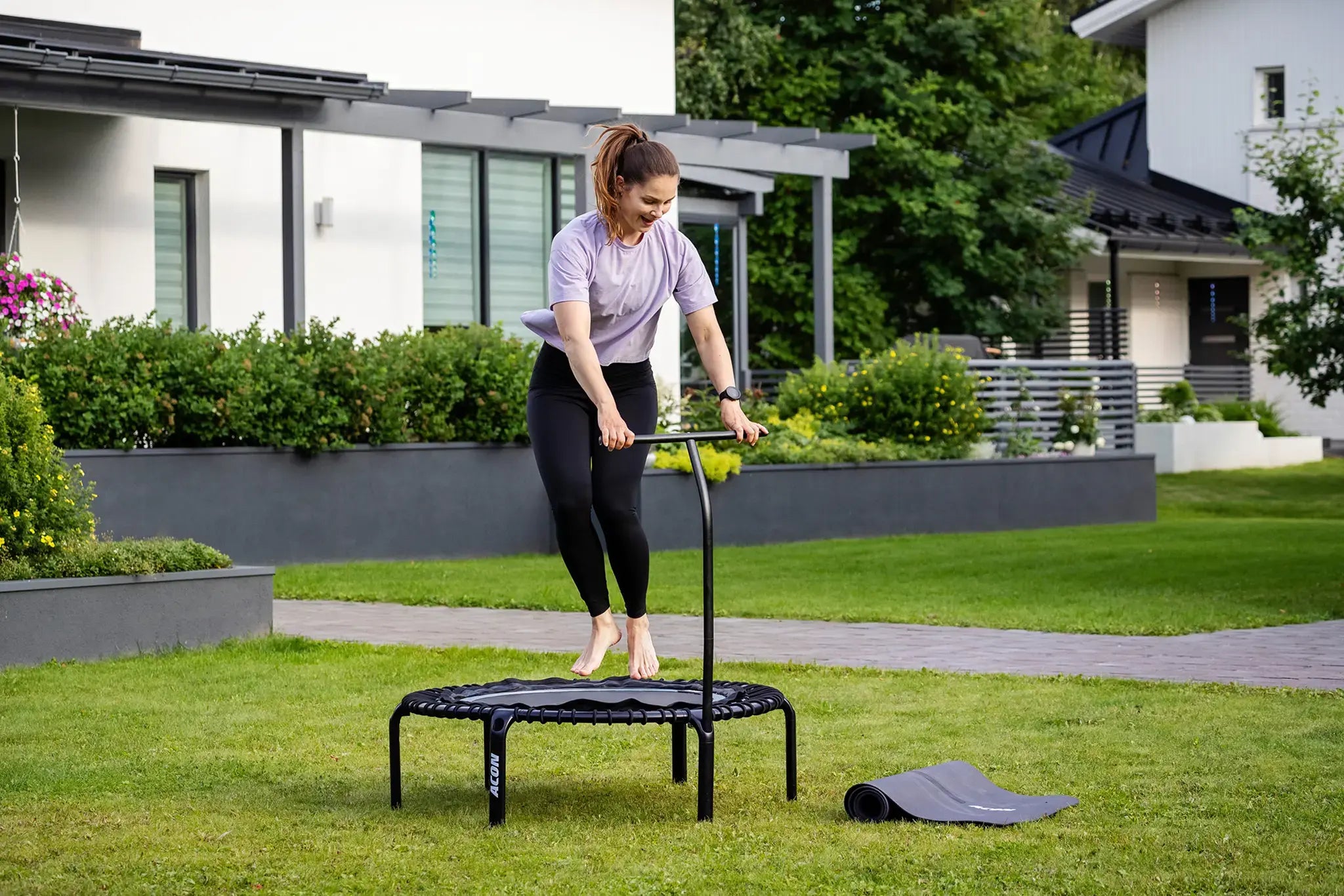 Woman jumping outside on an Acon rebounder trampoline with handlebar.