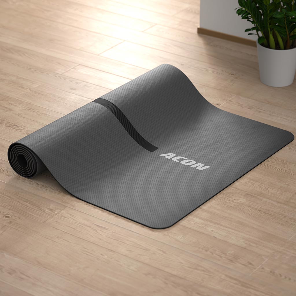 An image of a black yoga mat by ACON half-rolled on the floor
