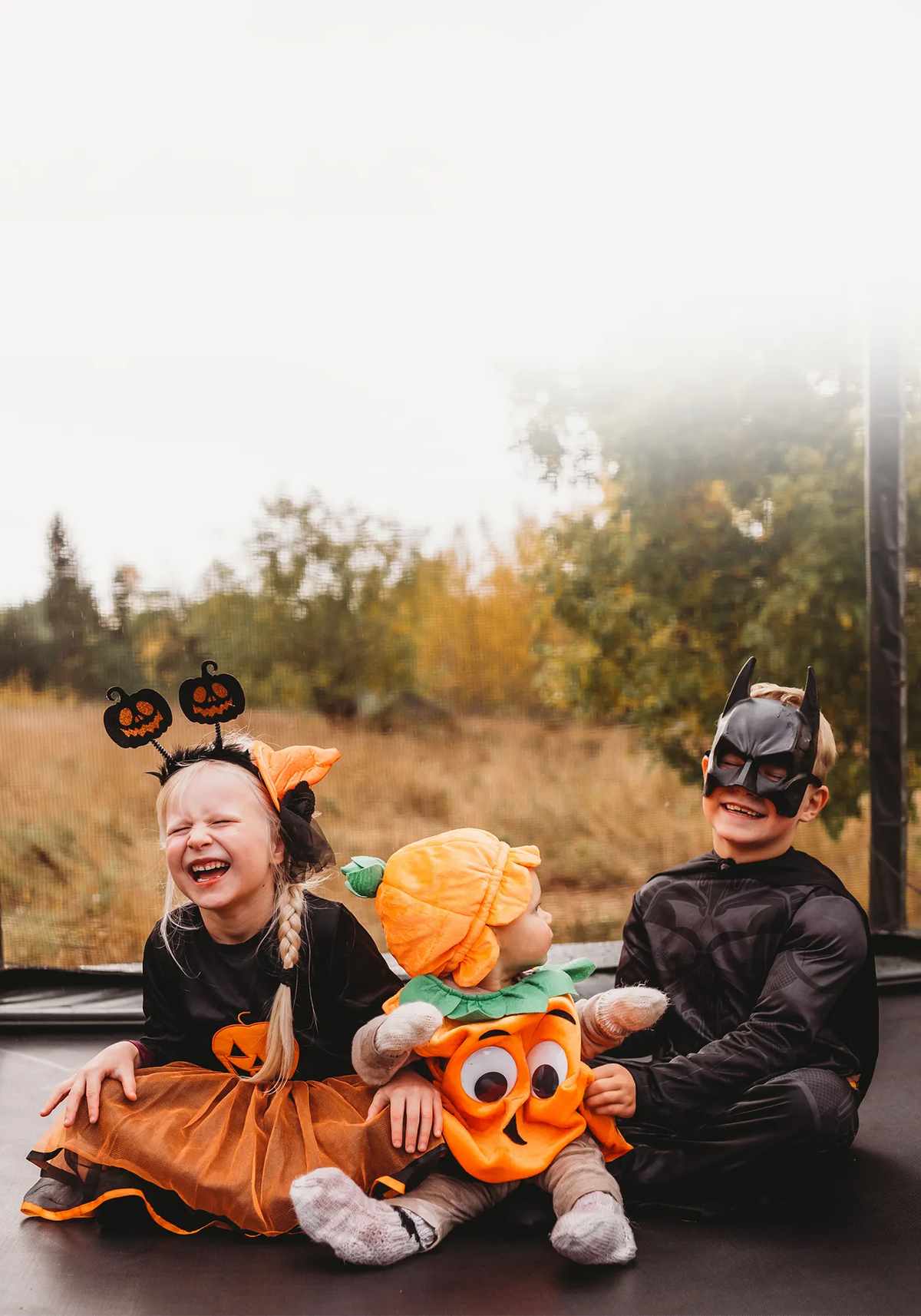 Three children in Halloween costumes sitting together on an ACON 16HD trampoline.