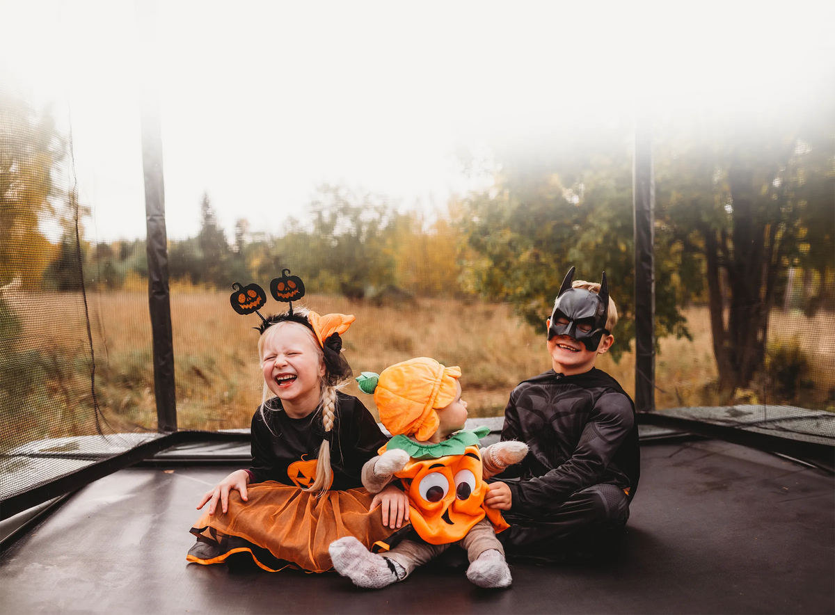 Three children in Halloween costumes sitting together on an ACON 16HD trampoline.