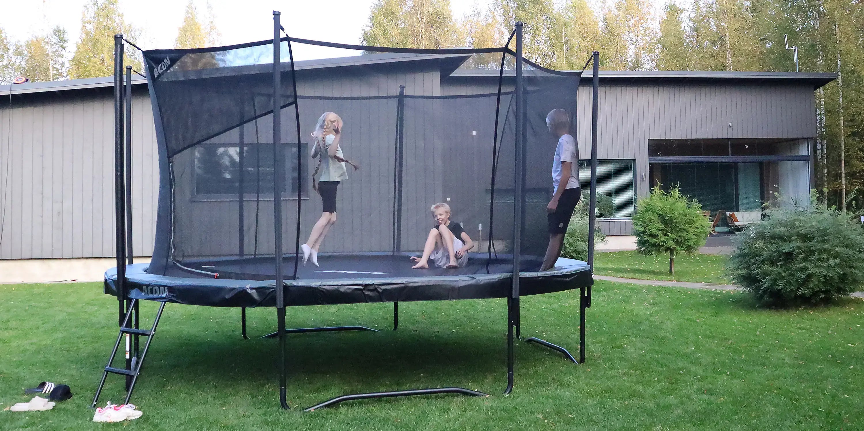 Three children jumping on an Acon 14ft round trampoline in a sunny backyard, showing how big a 14ft trampoline is.