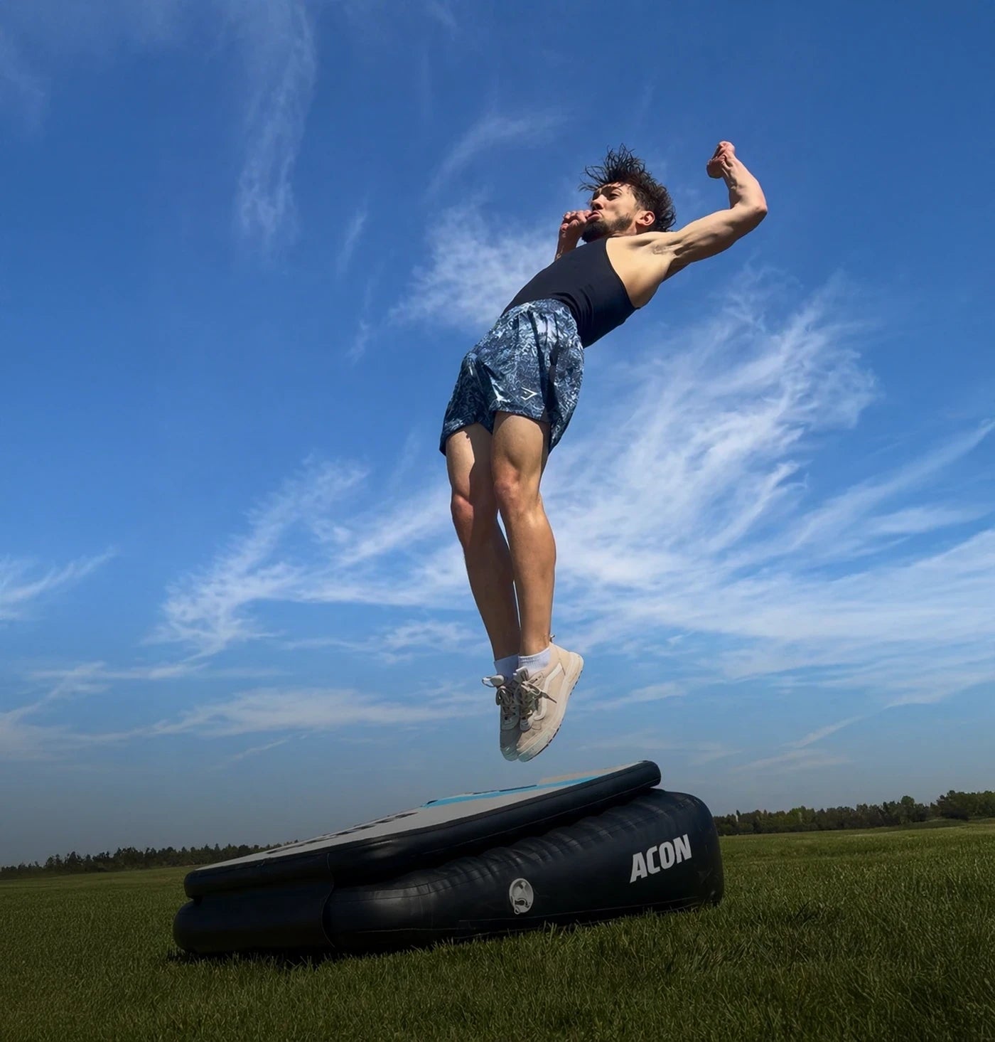 Man performing a Backflip Launch on an Acon Airboard outdoors, the Airboard placed on grass.