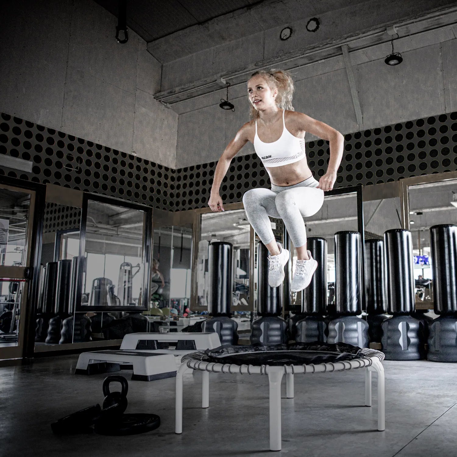 Athlete performing a jump on the ACON Fit 44in Round Rebounder with Active Handlebar inside a gym.