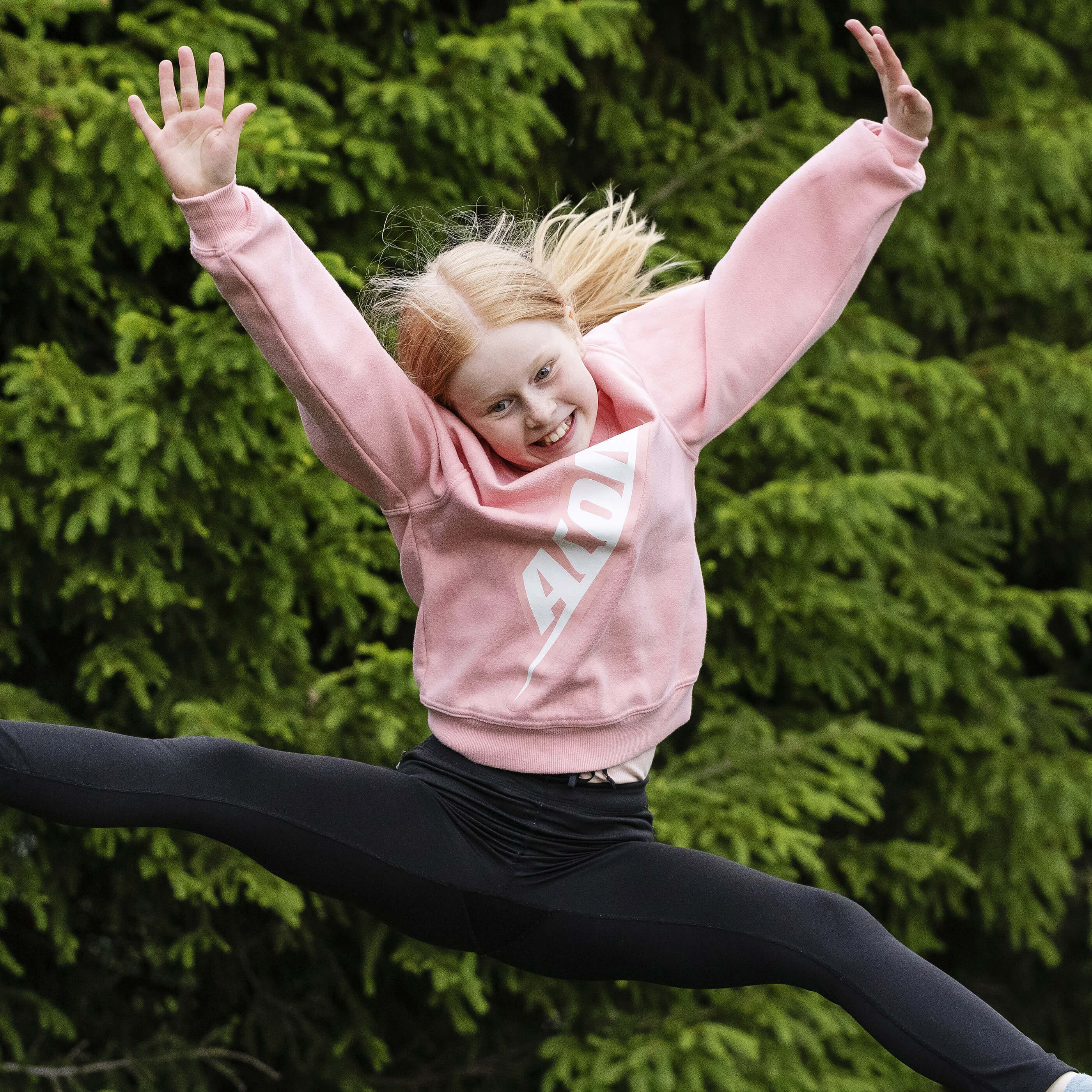 A happy girl in an Acon shirt jumping on a trampoline.