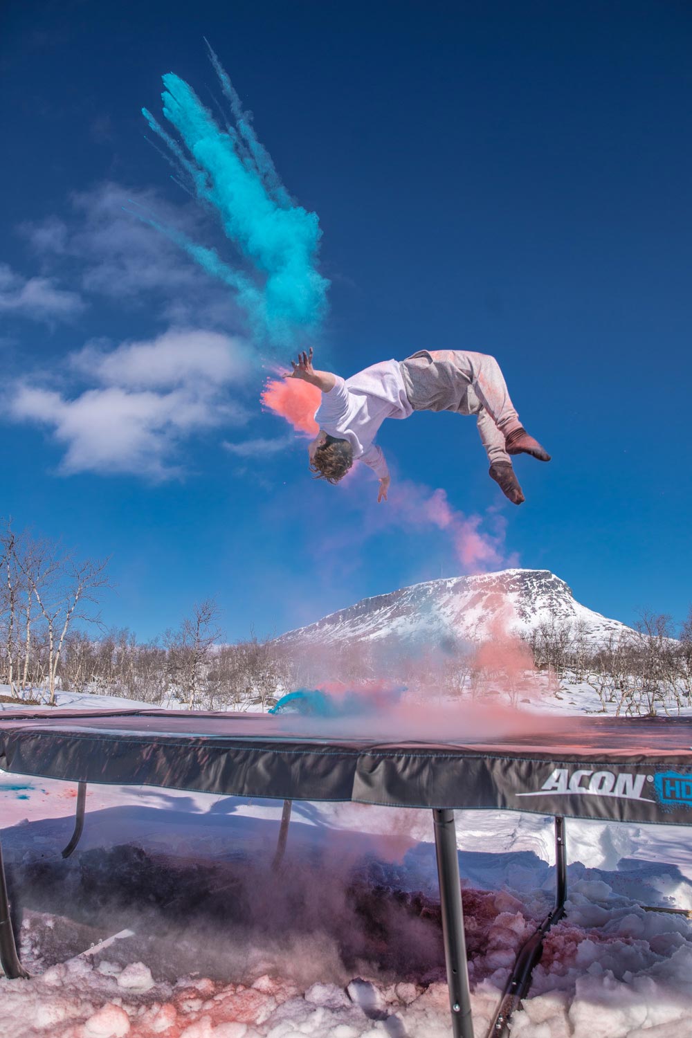 A person jumping on an ACON trampoline in Lapland, Finland, while there are red and blue colors in the background 