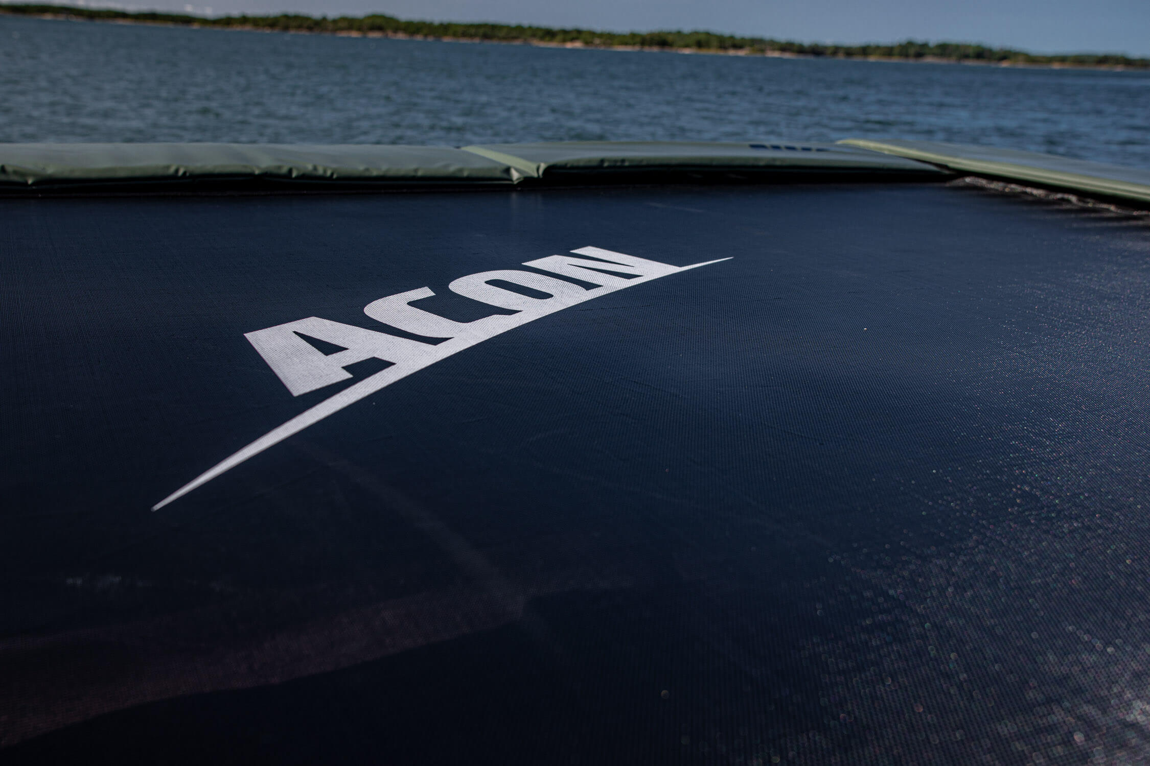 A close-up of ACON trampoline mat. The mat is black, the ACON logo is white and the paddings are green.