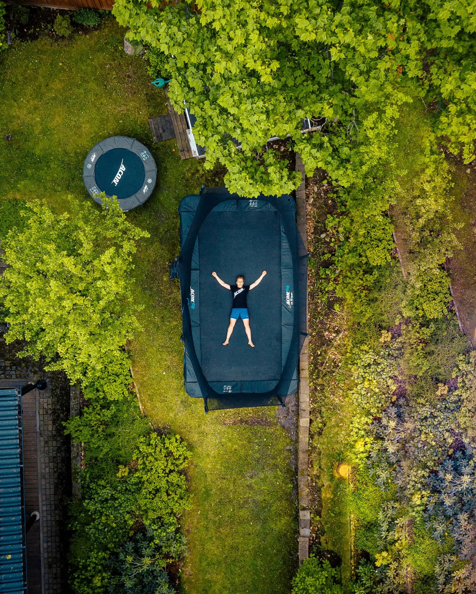 An aerial view of a boy lying on Acon 16 HD trampoline in a backyard.