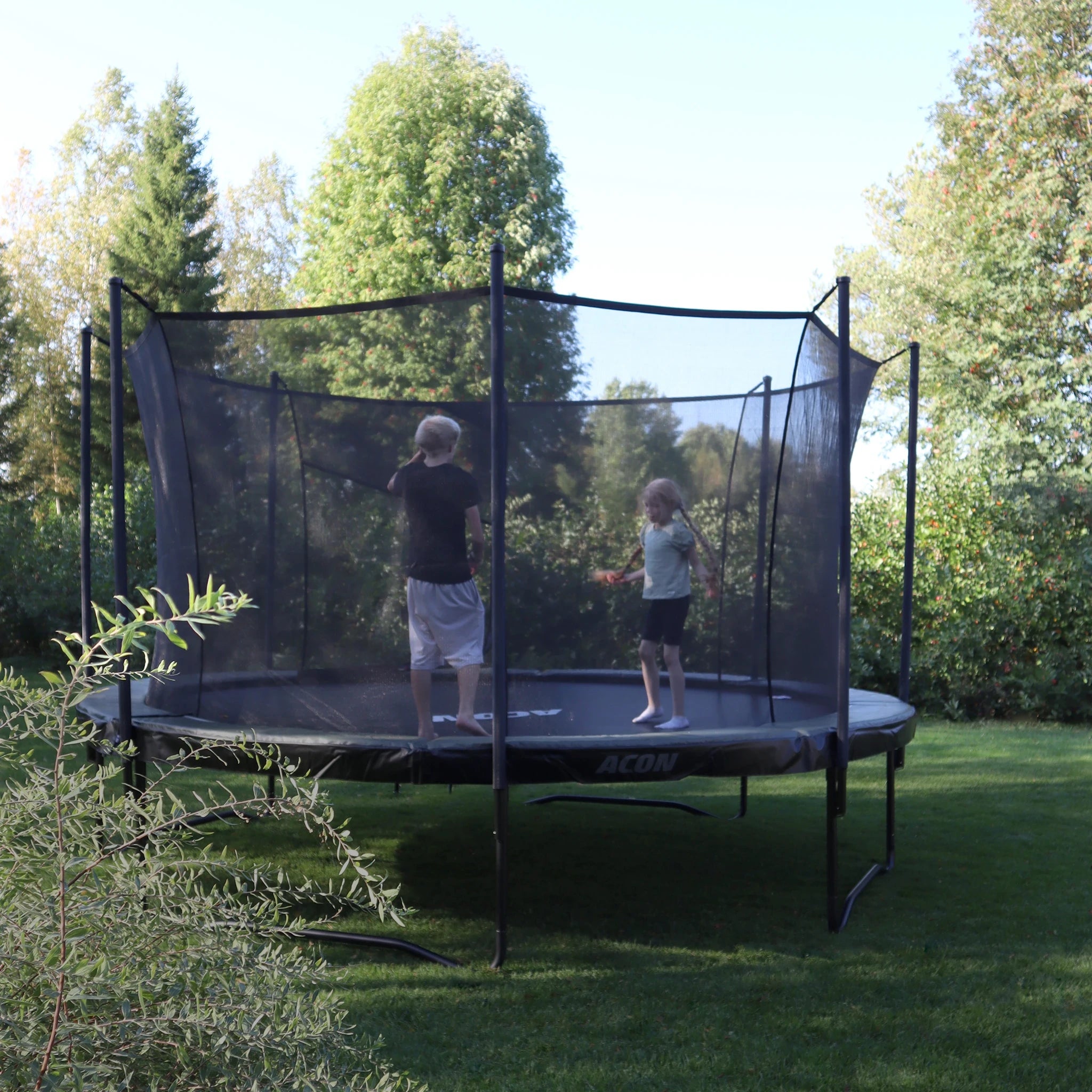 Acon Air trampoline in a summer backyard. Two children jumping on the trampoline.