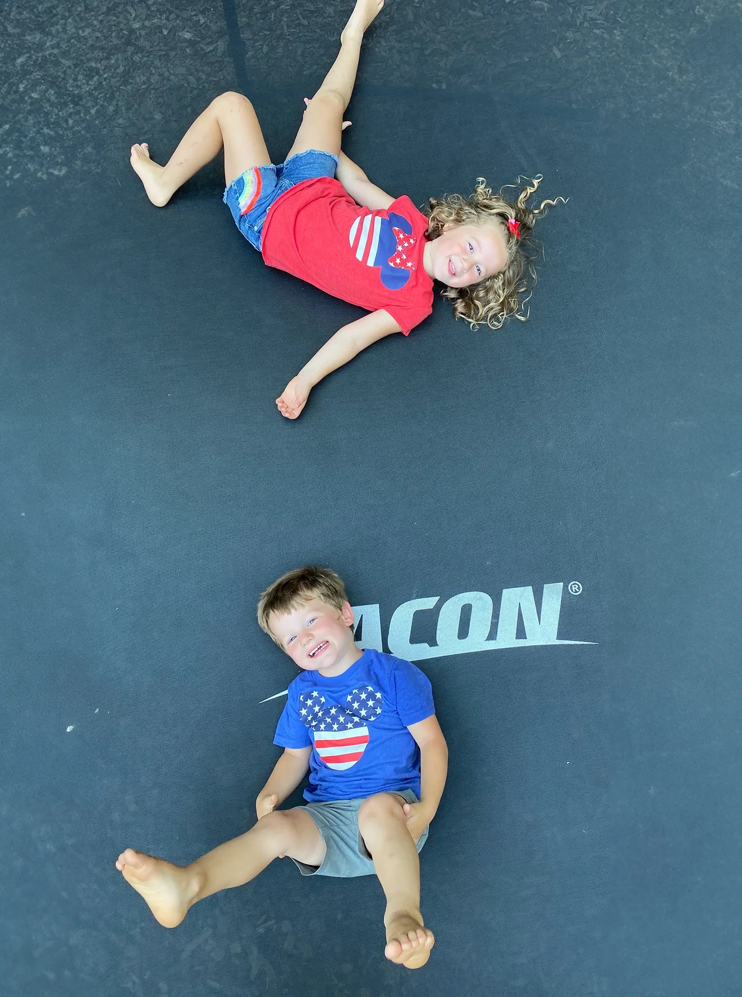 A happy boy and girl wearing America-themed t-shirts on an Acon trampoline.