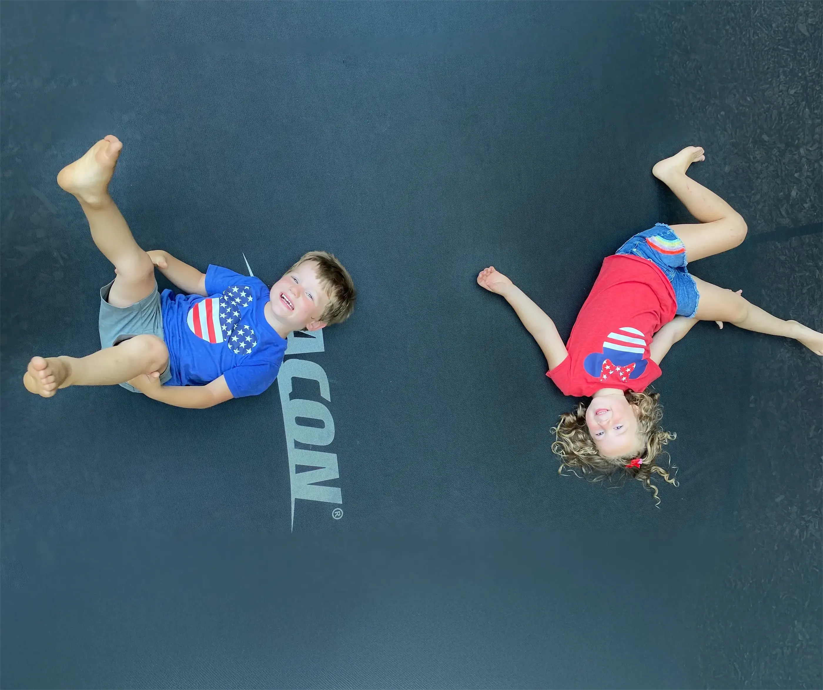 A happy boy and girl wearing America-themed t-shirts on an Acon trampoline.