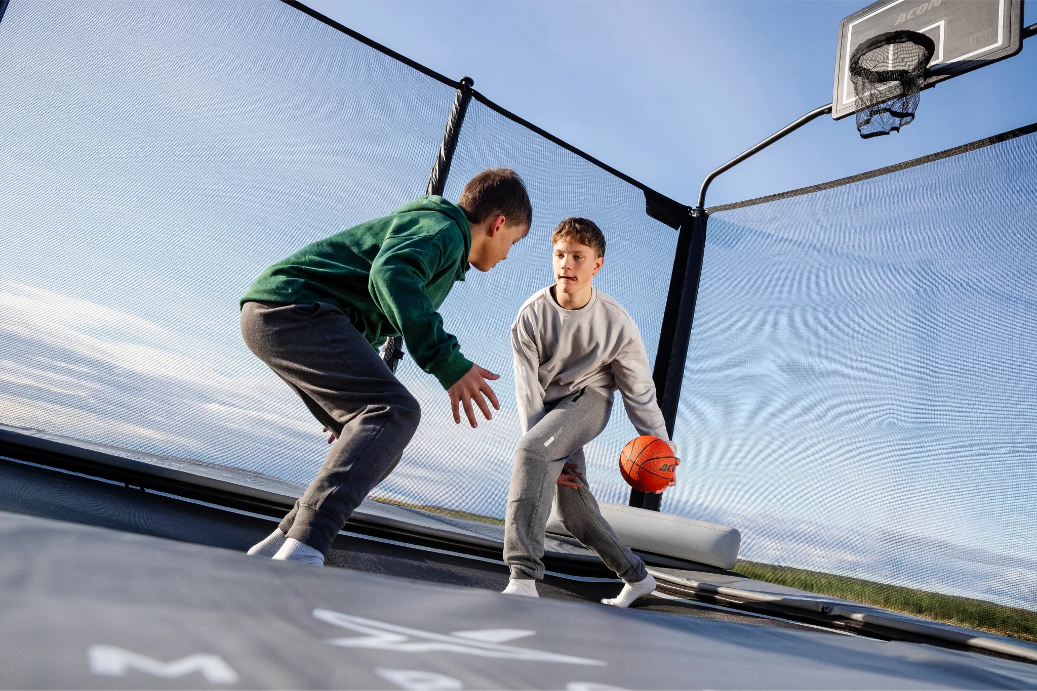 Teenagers playing basketball on an Acon X garden trampoline.