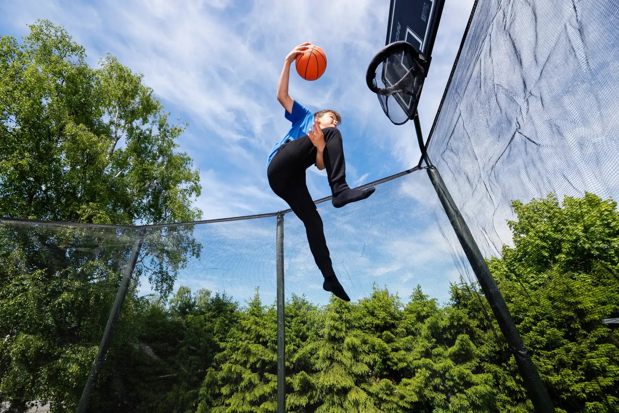 Child jumping on a trampoline while making a trick shot into a basketball hoop.