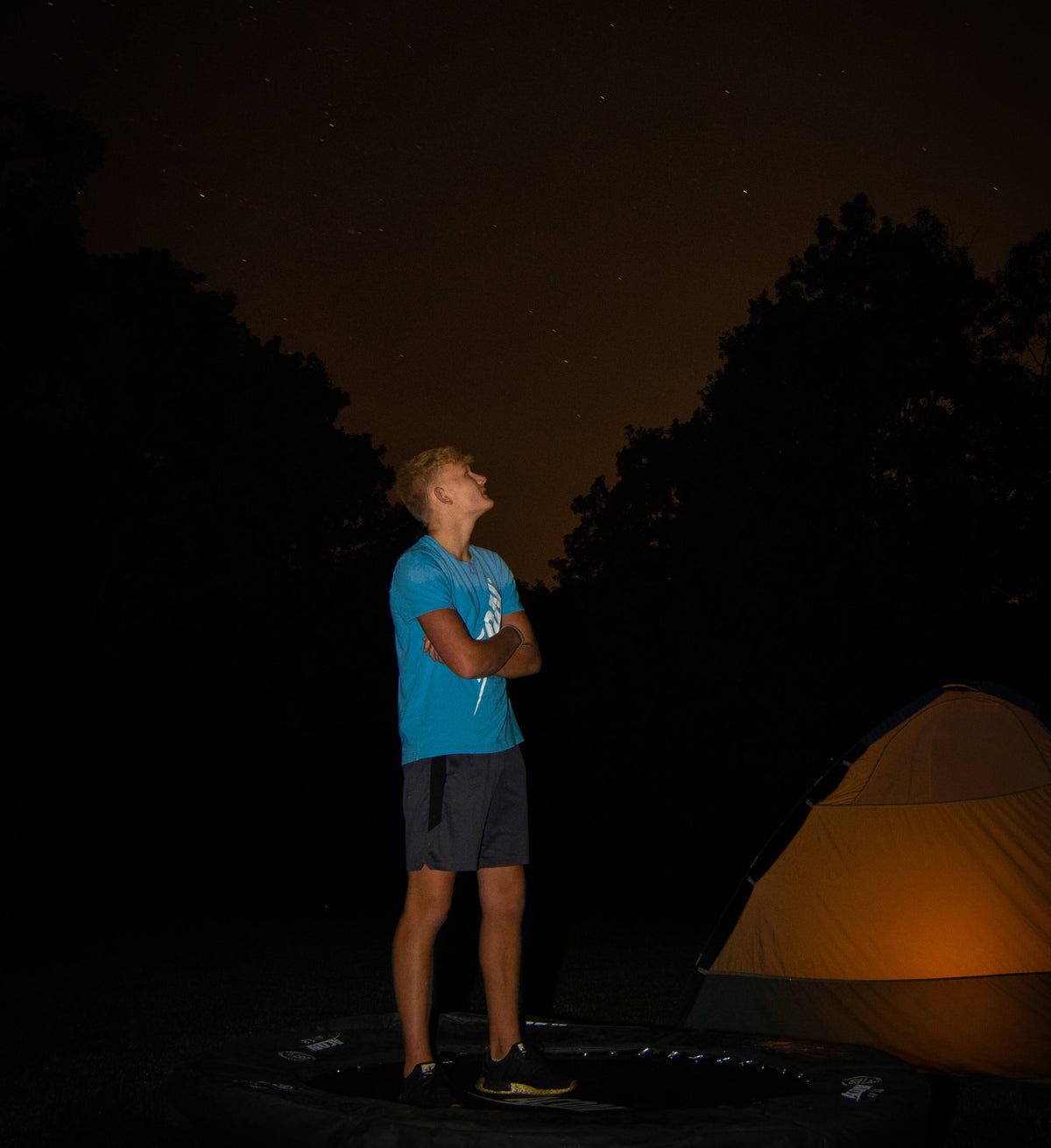 Boy standing on a trampoline and watching starry night sky.