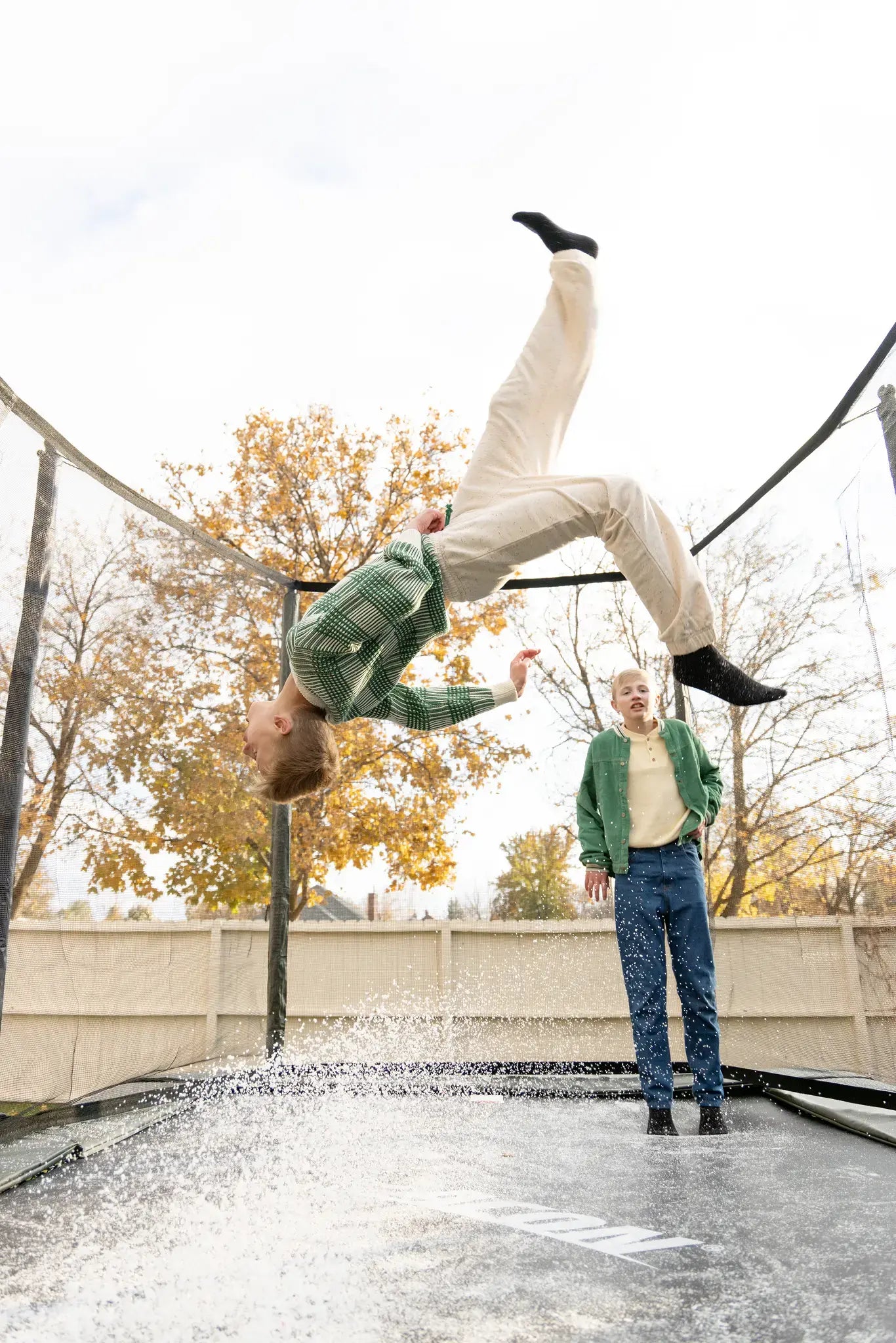 Teenager boy performing a backflip on an Acon trampoline in winter, while other boy watches in the background.