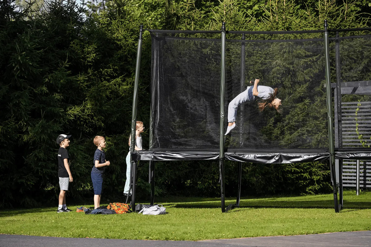 Girl performing a trampoline trick while friends watch from the backyard.