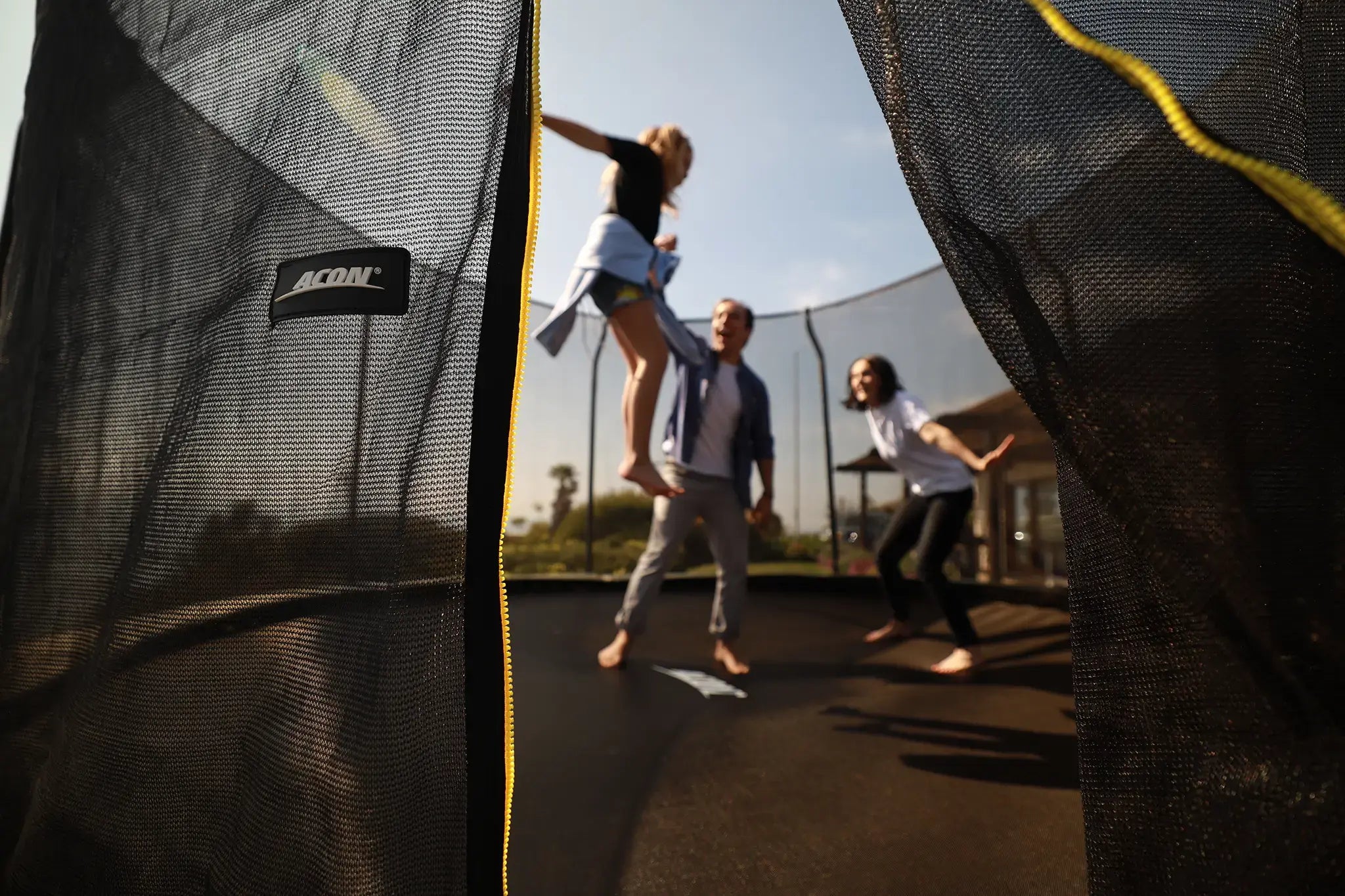 Family playing together on a Acon trampoline, seen through the safety net.