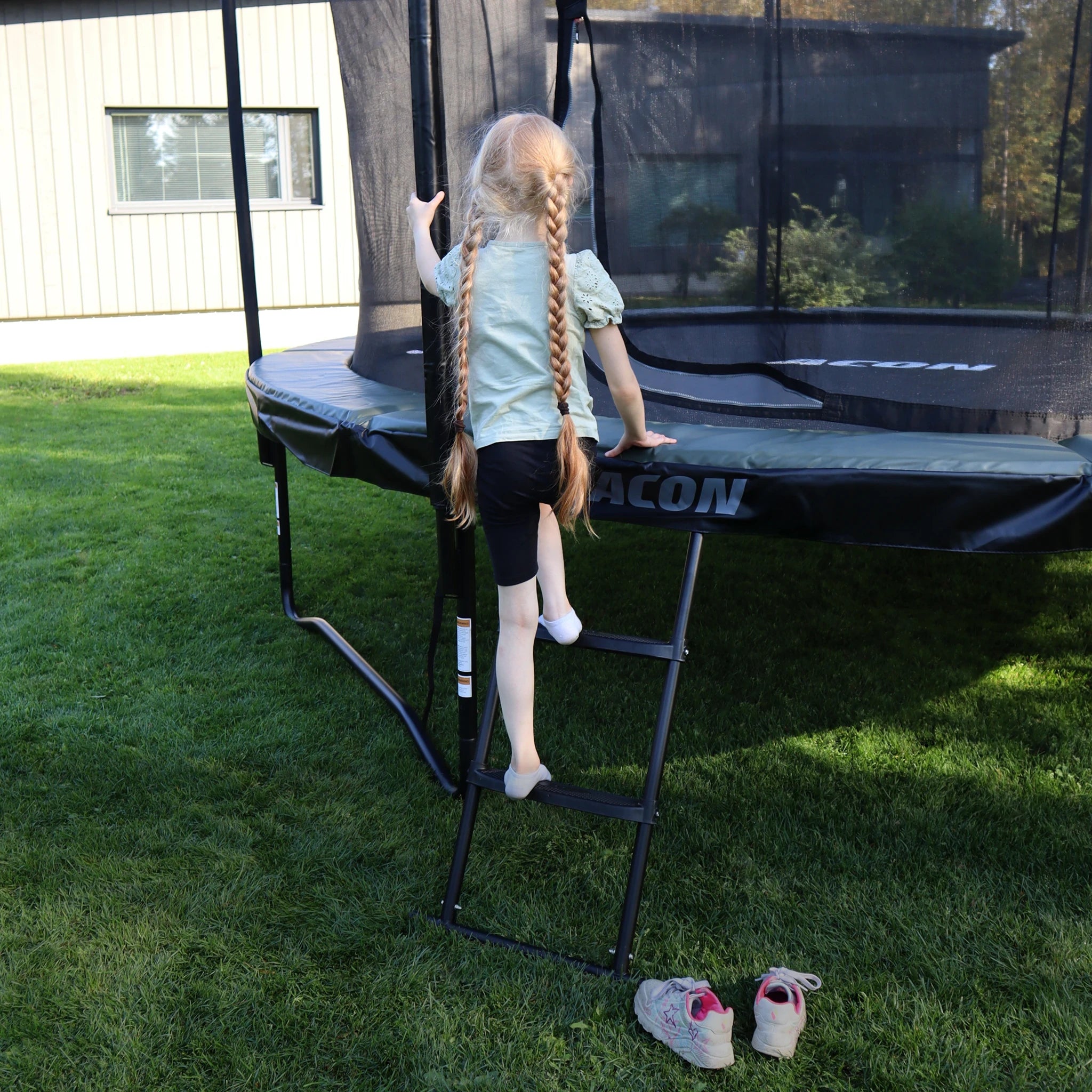 A little girl climbs the ladder to an Acon Air trampoline while holding the safety net pole with one hand.
