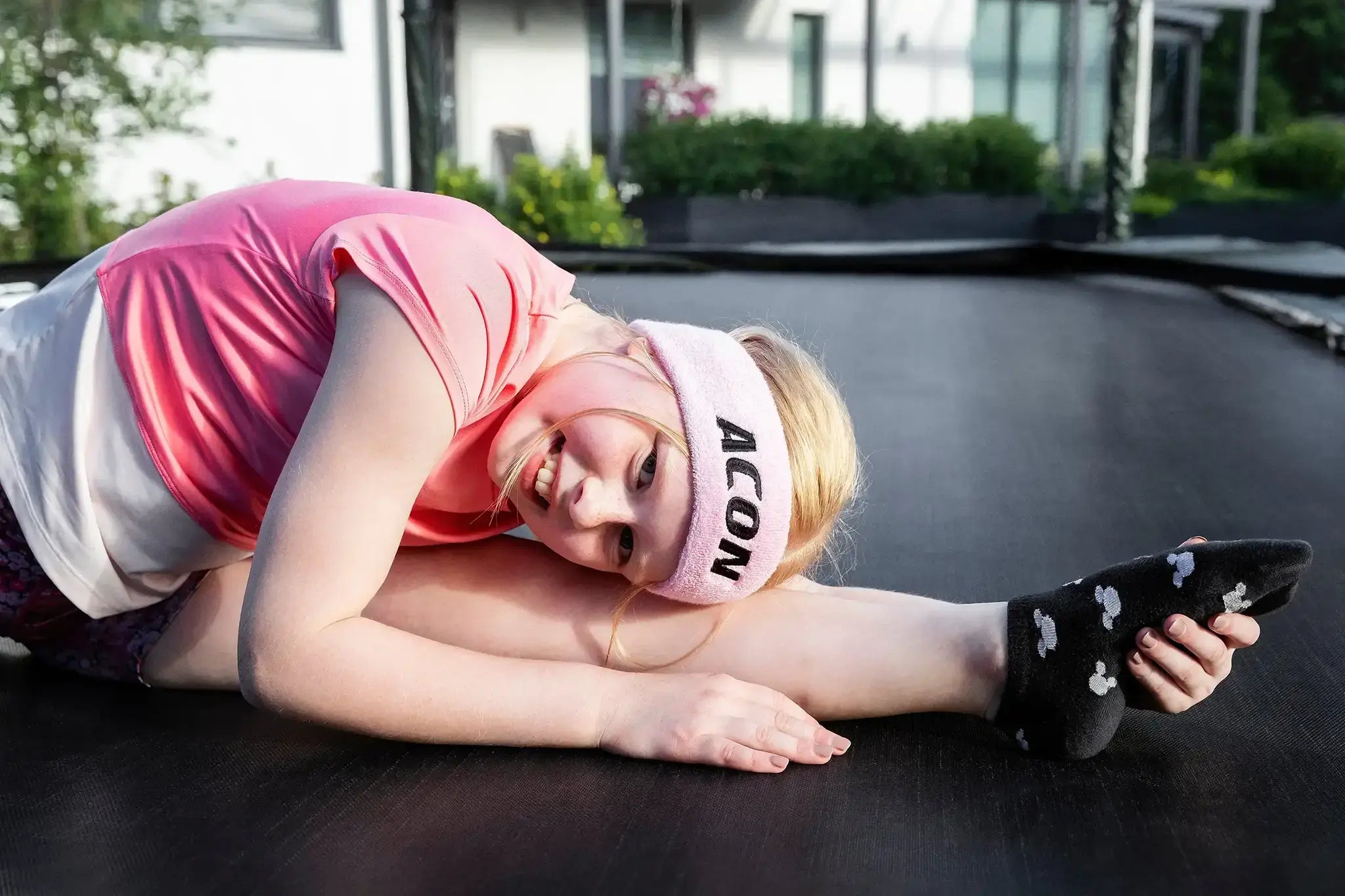 Girl with a pink Acon headband stretching on a trampoline.