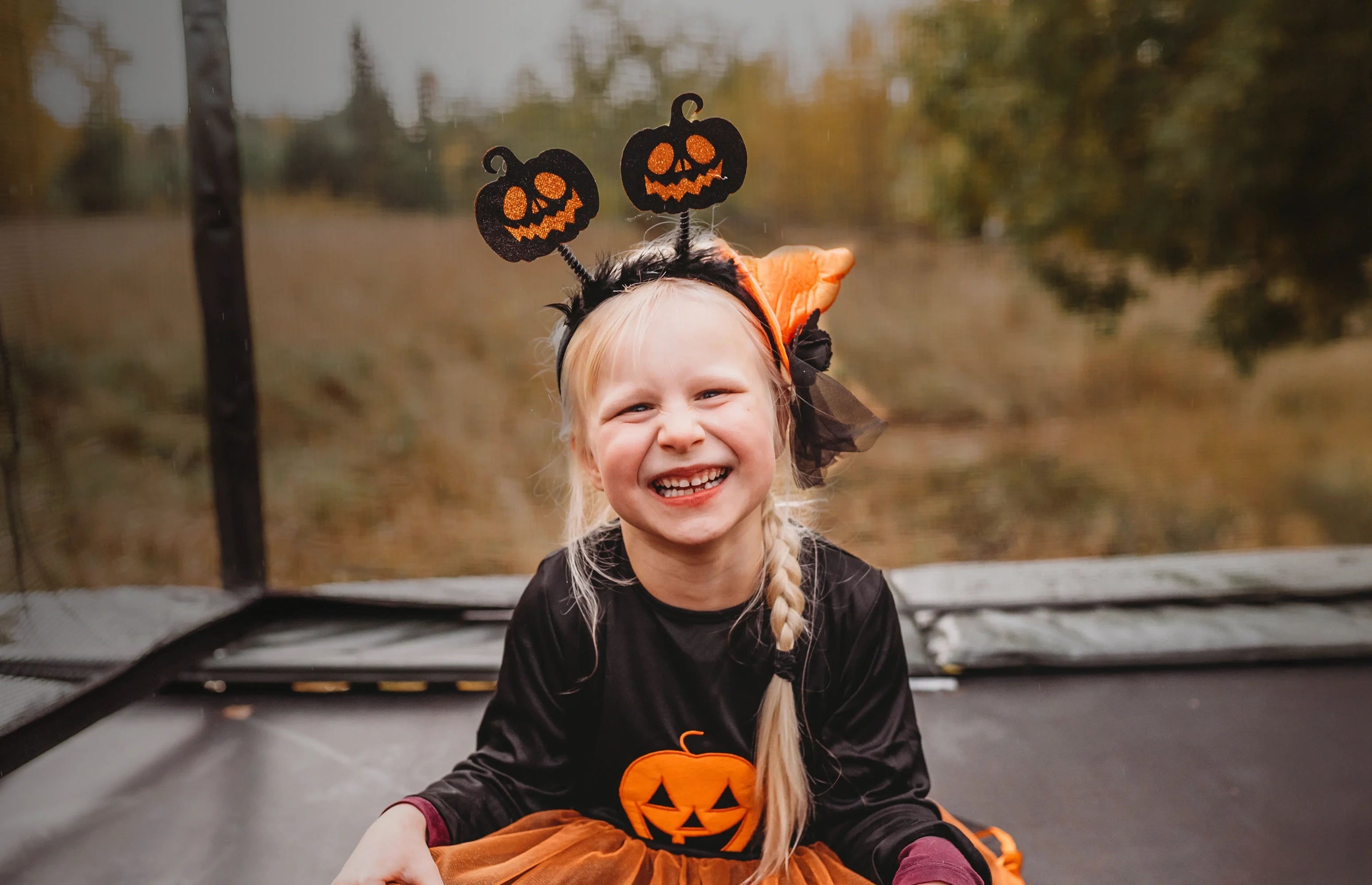 Child wearing a Halloween costume with pumpkin design sitting on an Acon HD trampoline outdoors.