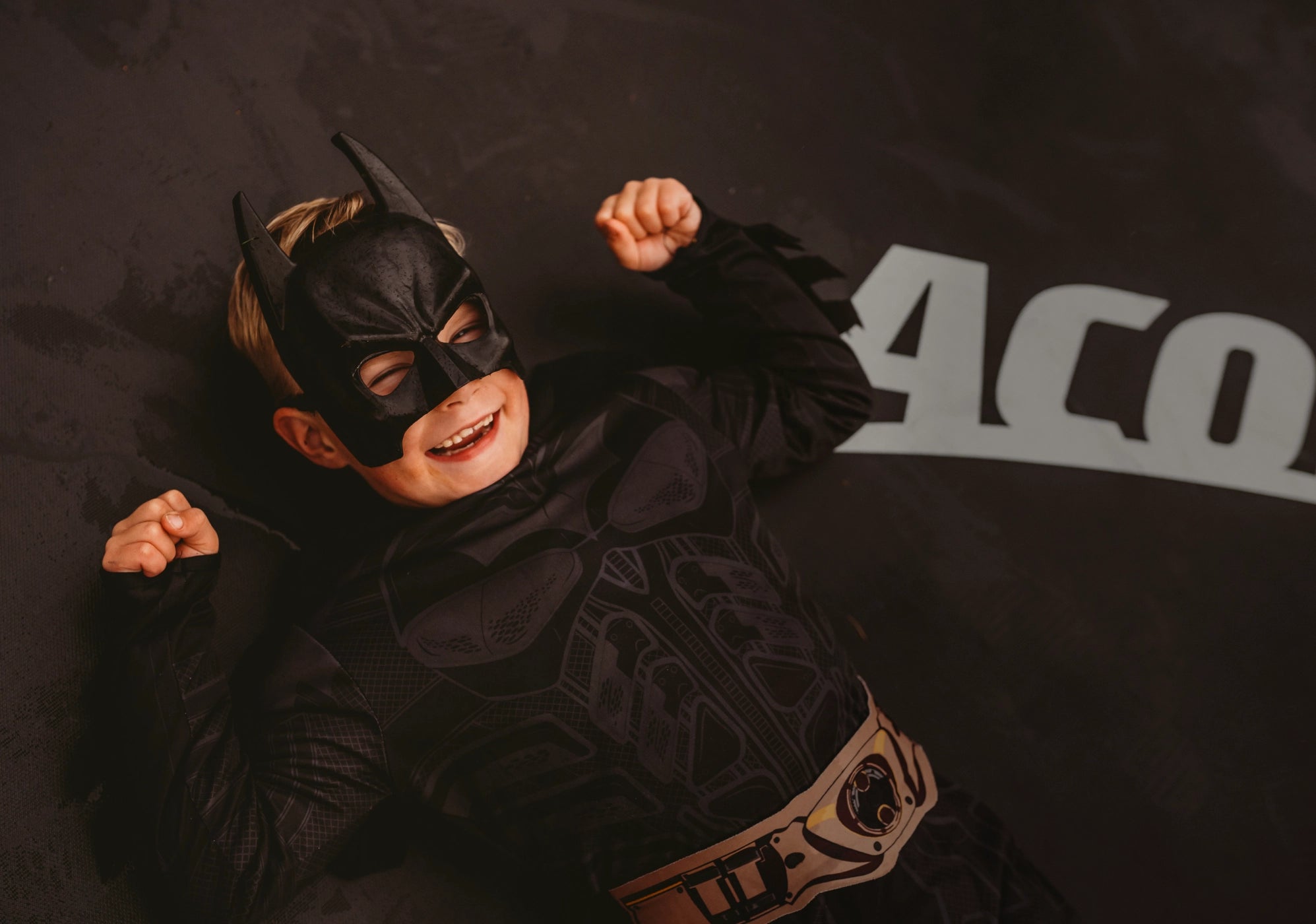 A boy dressed as Batman lying on an Acon trampoline.