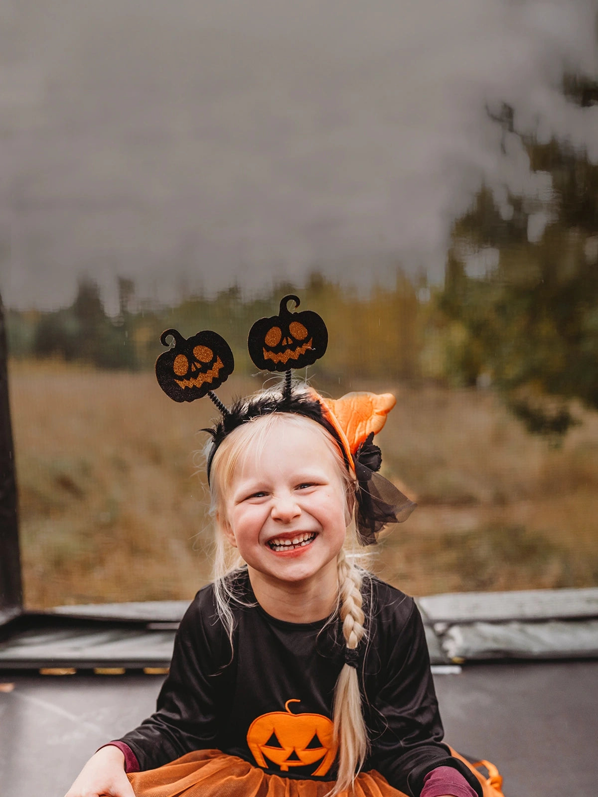 Child wearing a Halloween costume with pumpkin design sitting on an Acon HD trampoline outdoors.