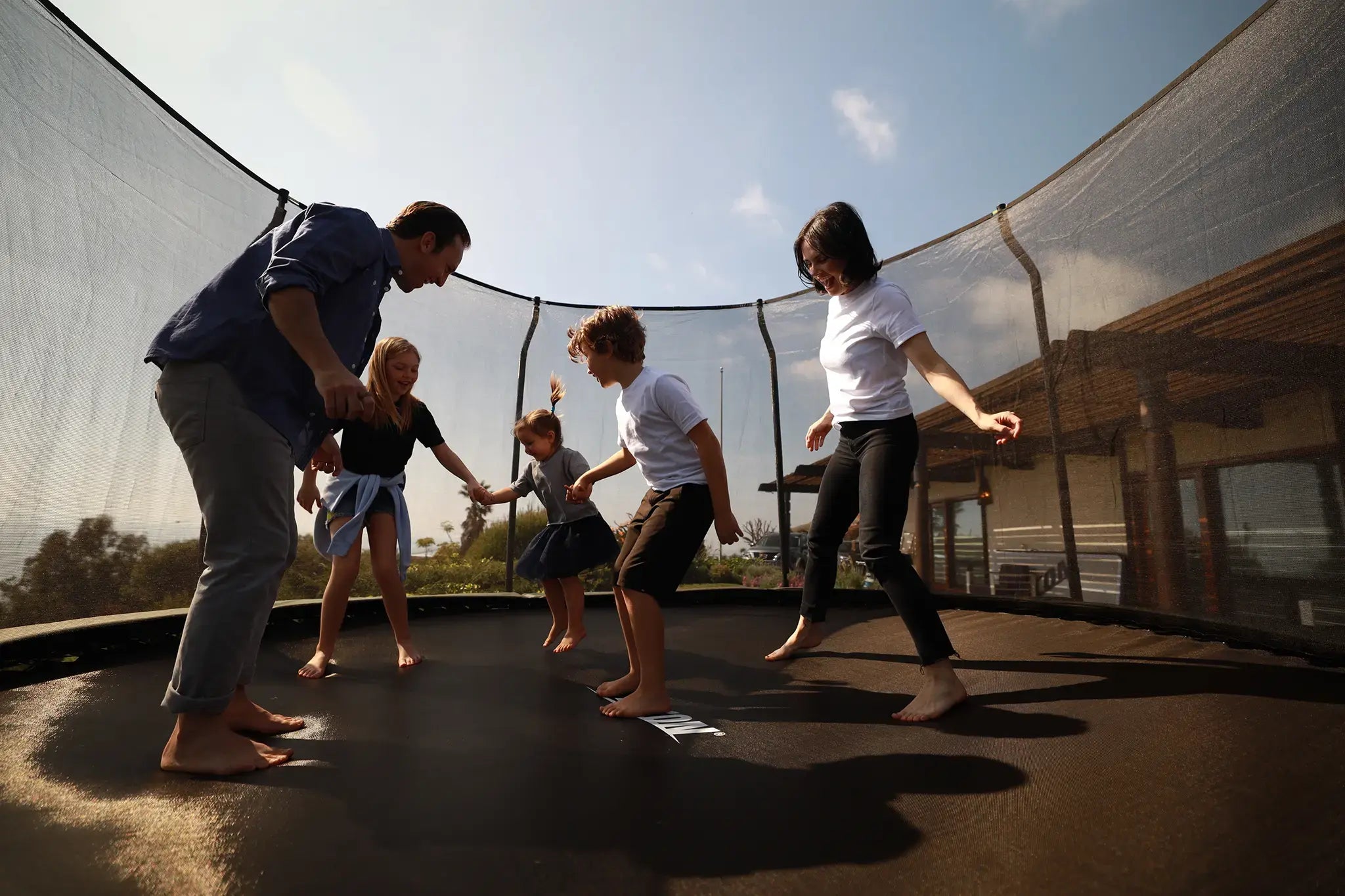 Happy family of mom dad and three children jumping together on a round Acon trampoline with safety net. 