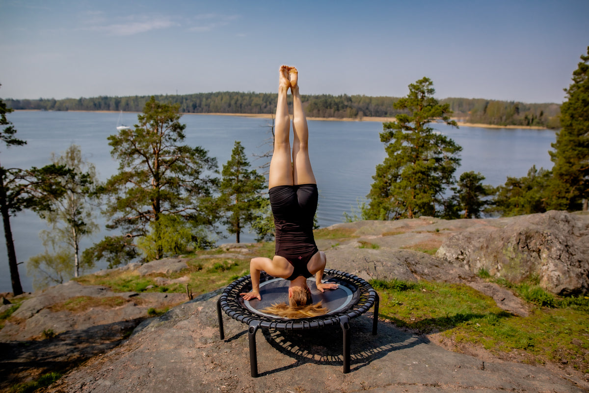 A woman doing a headstand on a rebounder trampoline by ACON