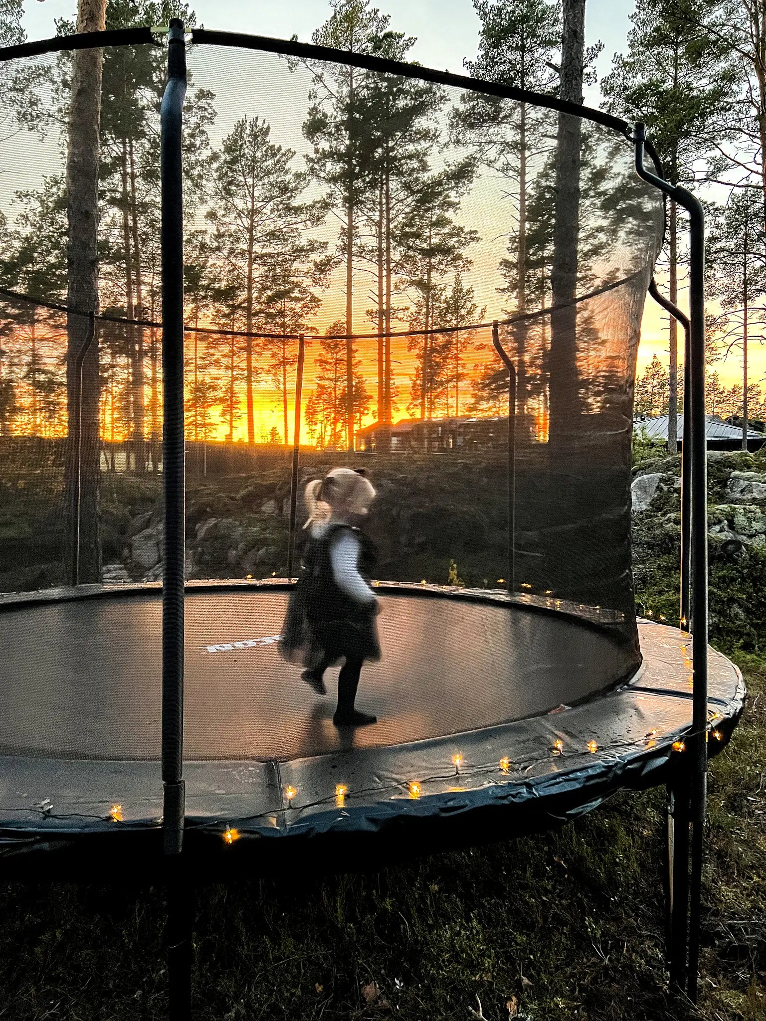 A little girl jumping on a round trampoline with enclosure.