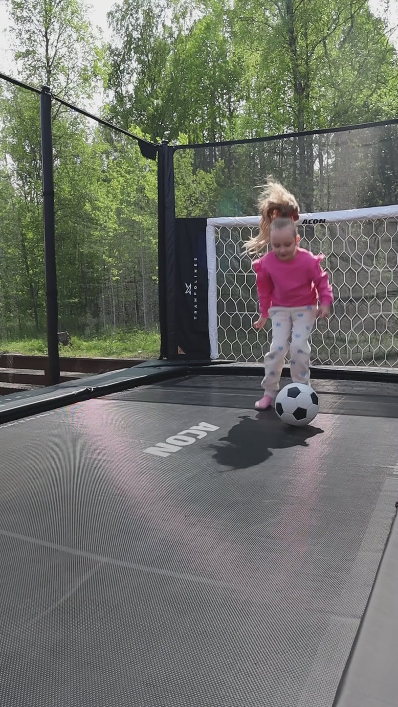 A little girl is bouncing on an Acon X trampoline and playing trampoline football.