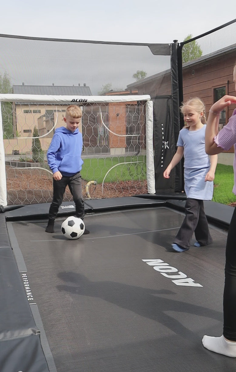 Three kids play football on an Acon X trampoline. Behind the goalie is the Acon X trampoline football goal.