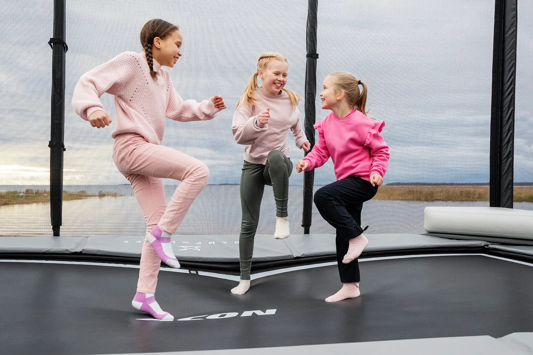 Three girls jumping happily on a rectangular Acon trampoline with safety net. 