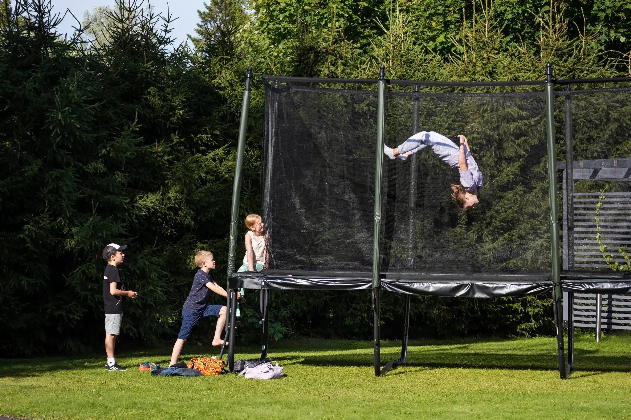 A child doing a backflip on a trampoline with a safety net. Other kids are waiting their turn outside the trampoline.