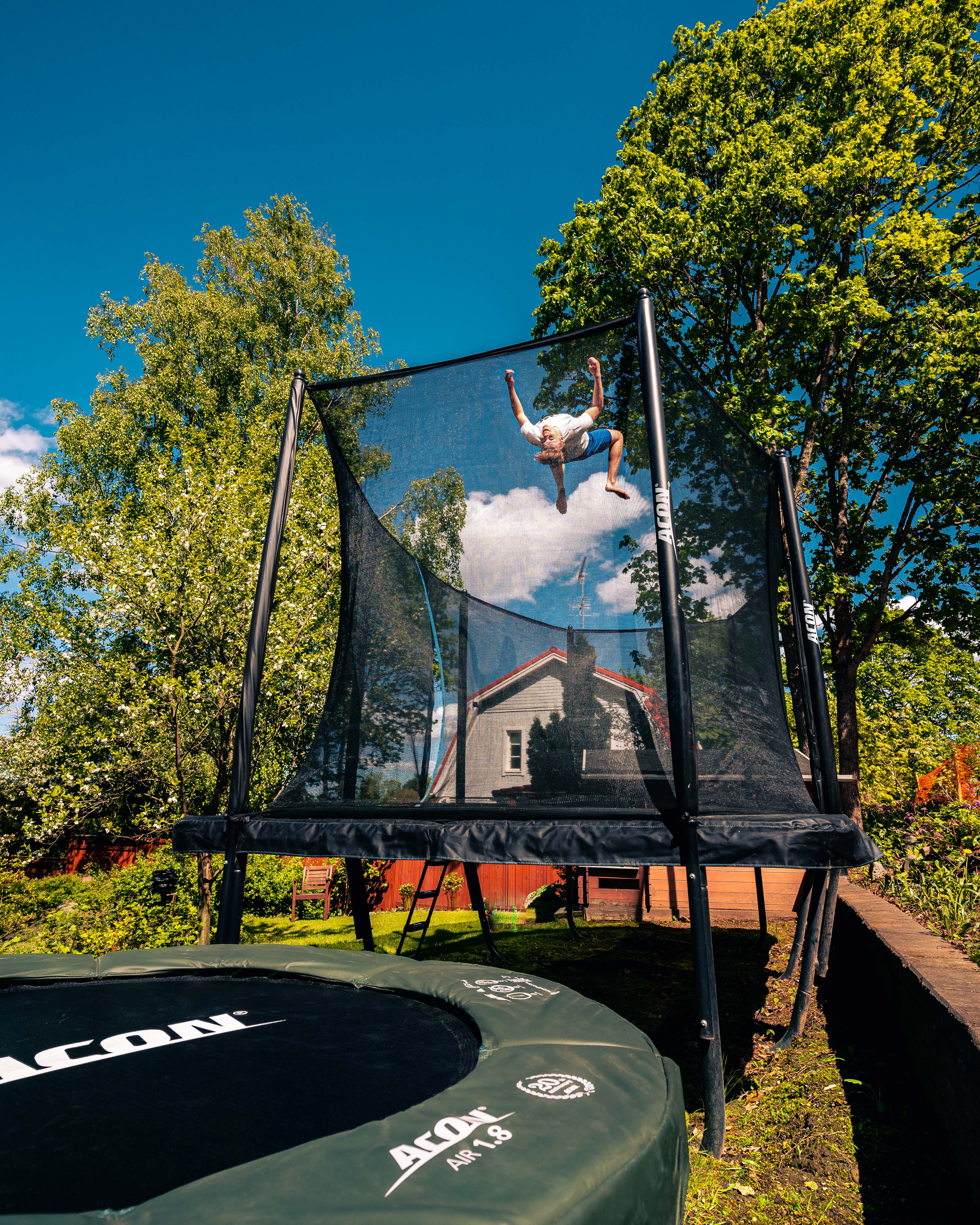 A guy doing a backflip on an ACON rectangular trampoline with net
