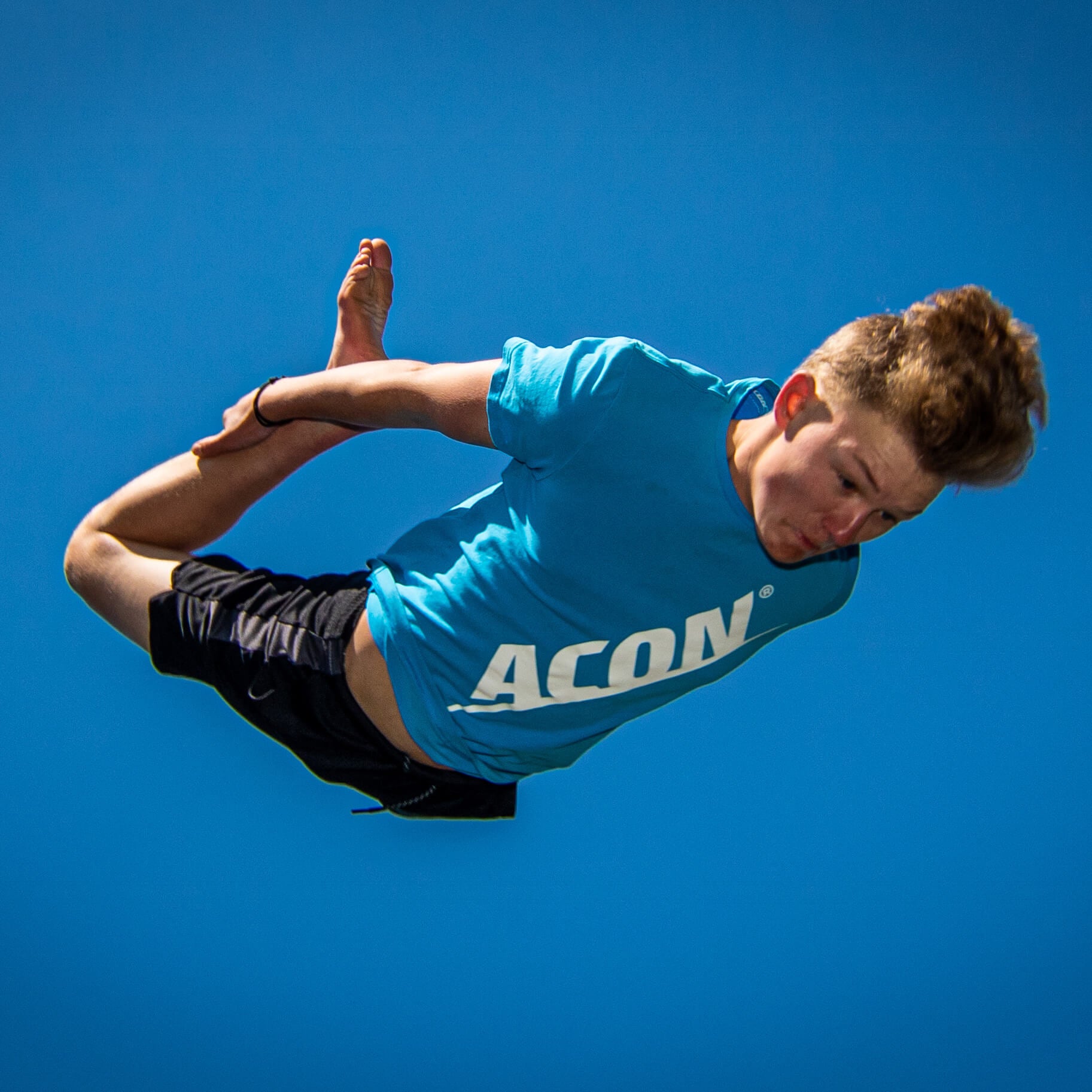 A boy in a blue acon t-shirt doing a trampoline jump.